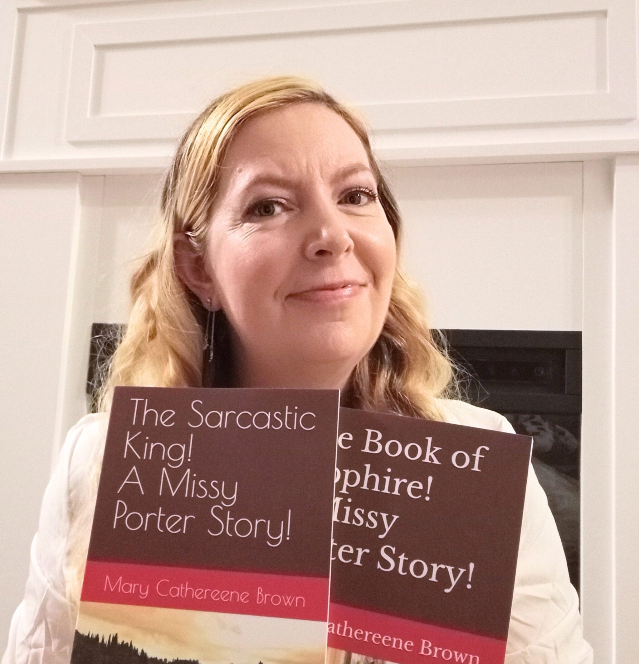 This photograph shows Mary holding two books from her Missy Porter series. Mary has long blond hair and is smiling at the camera. She is wearing a white long-sleeve shirt.